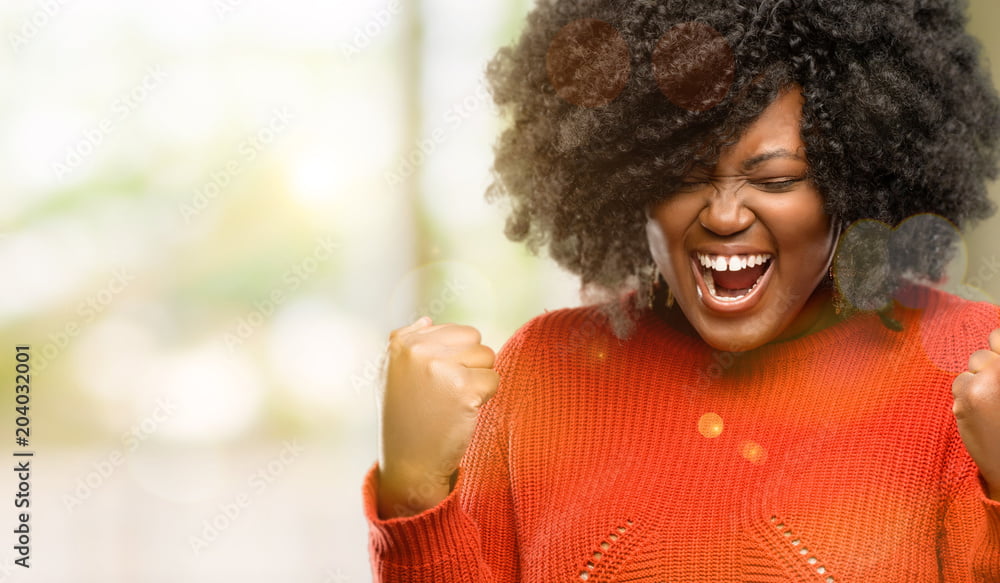 Beautiful african woman happy and excited celebrating victory expressing big success, power, energy and positive emotions. Celebrates new job joyful, outdoor