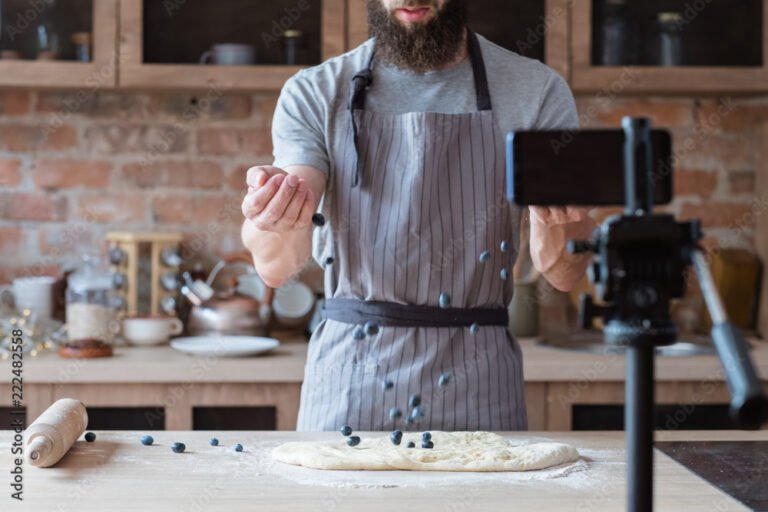 content creation for social media. food blogger in apron shooting video of himself using camera on tripod. modern technology and freelance work concept. man preparing blueberry pie.