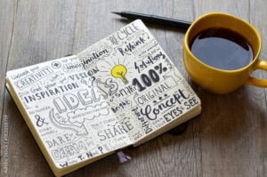 Handwritten sketch notes IDEAS in notepad on table with coffee and pen